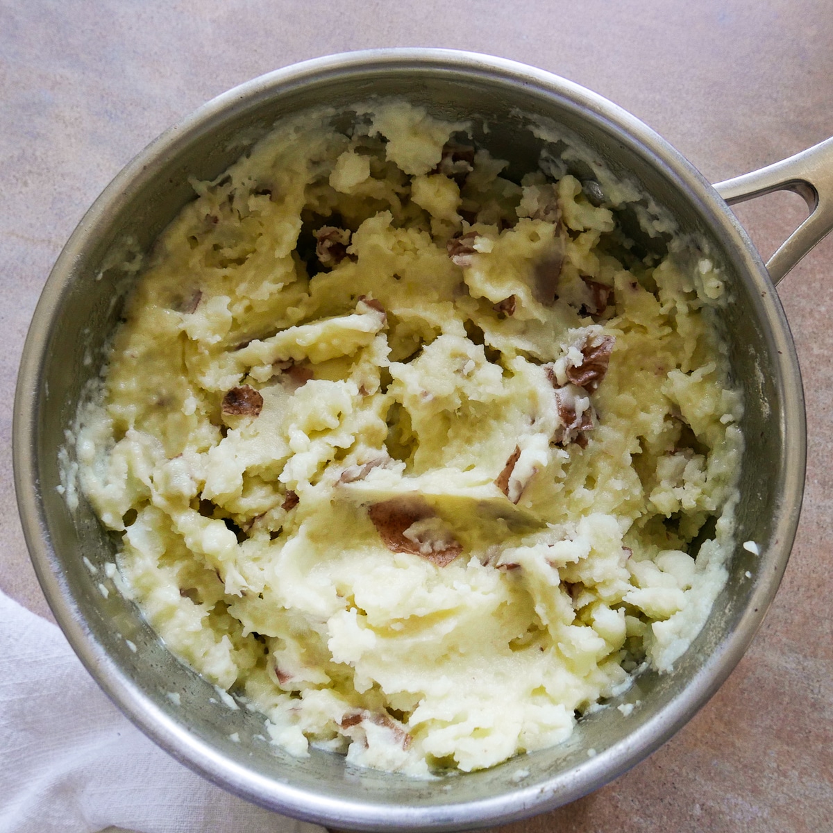 Mashed potatoes combined with garlic butter and half & half in a saucepan.