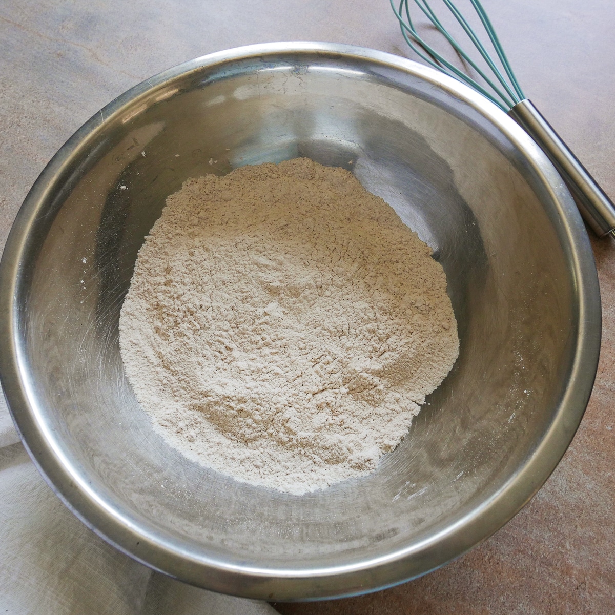 dry ingredients whisked together in a mixing bowl with a whisk in the background. 