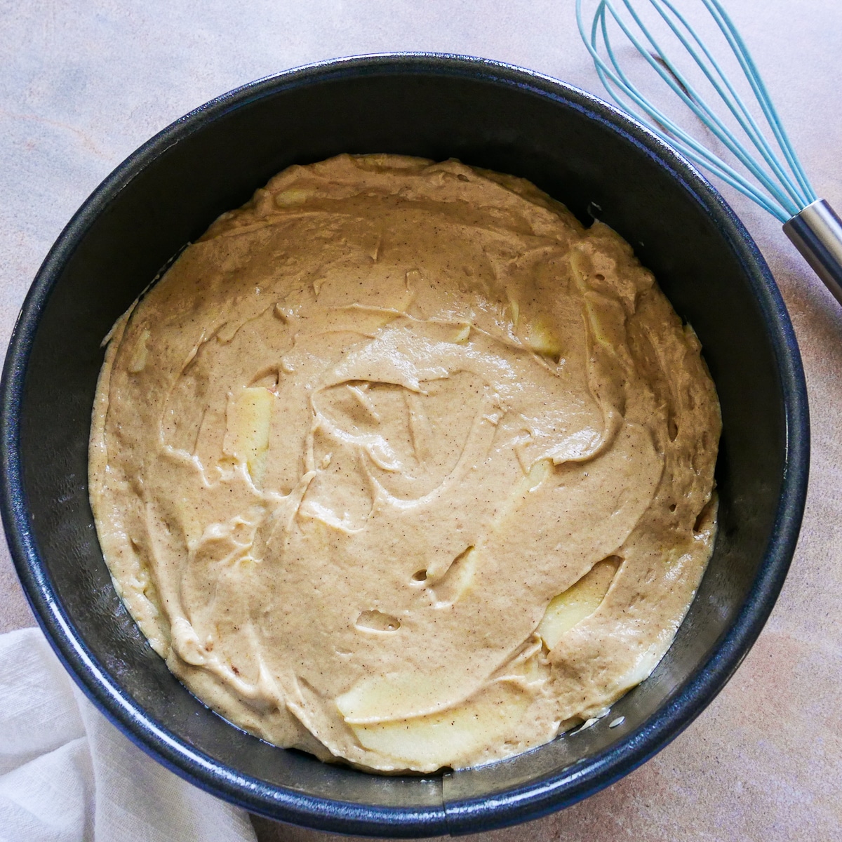 Sliced apples mixed into cake batter and poured into a prepared springform pan.