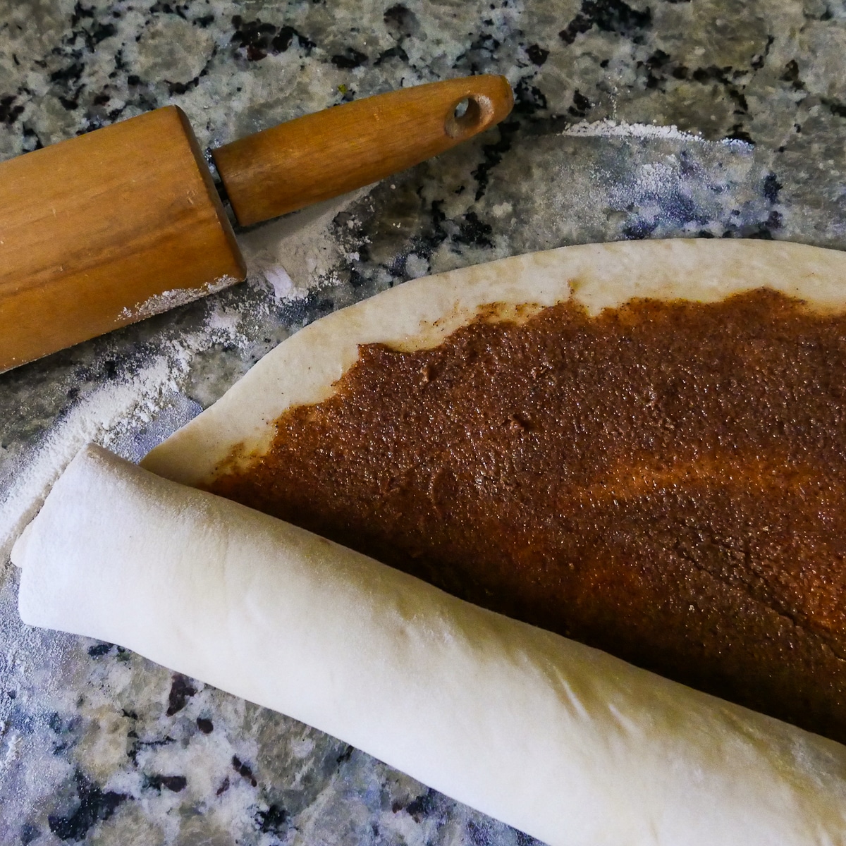 Rolling up dough into a log with rolling pin in the background. 