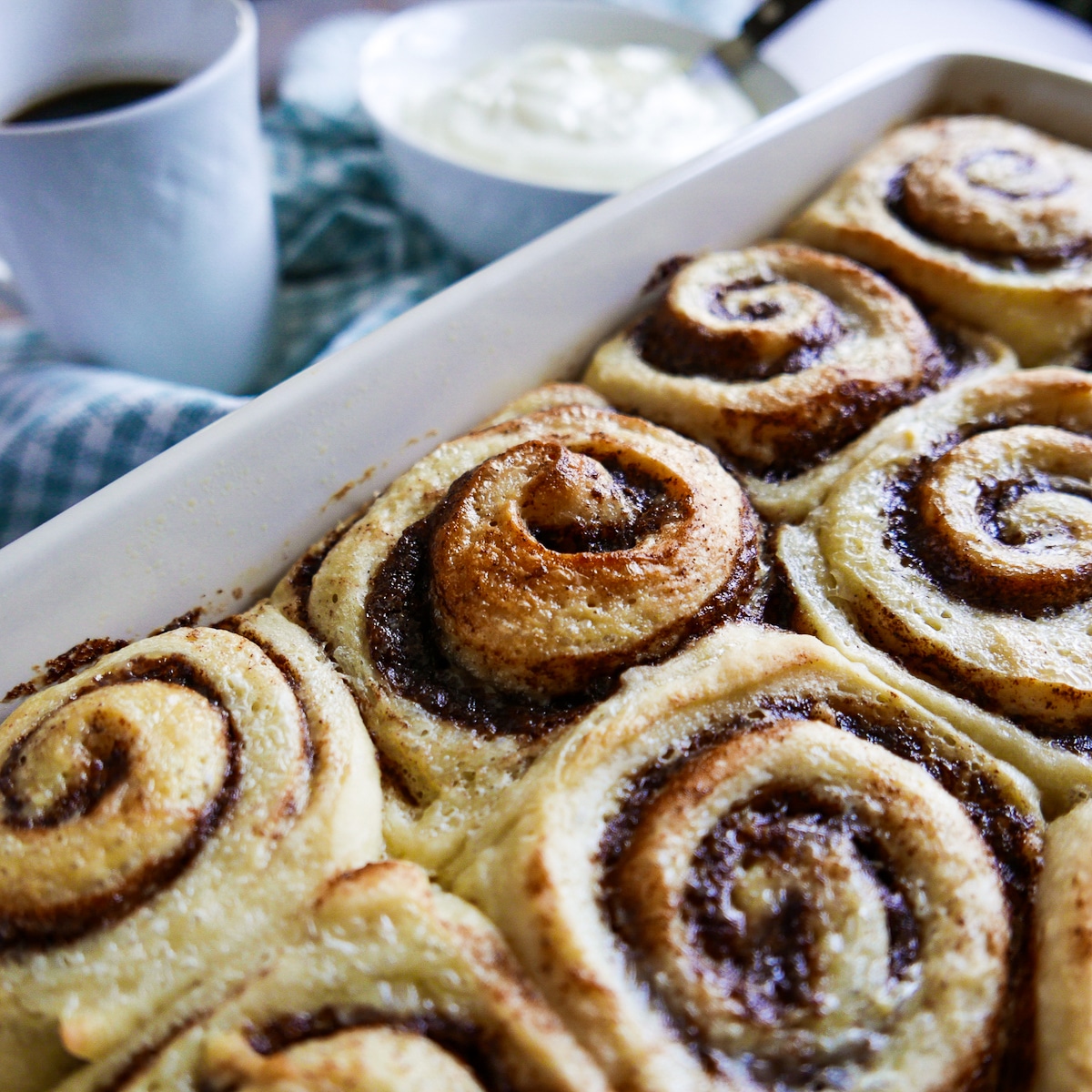 baked cinnamon rolls in a baking dish with cup of frosting in the background. 