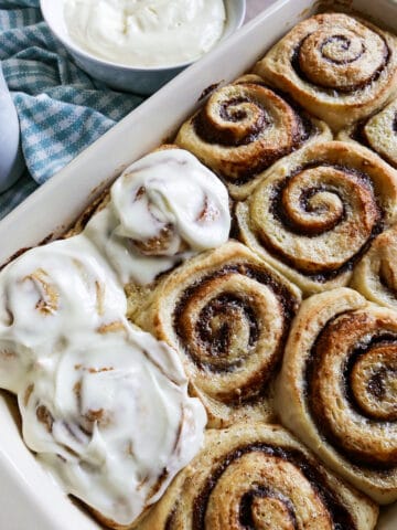 partially frosted pan of cinnamon rolls with cup of coffee.