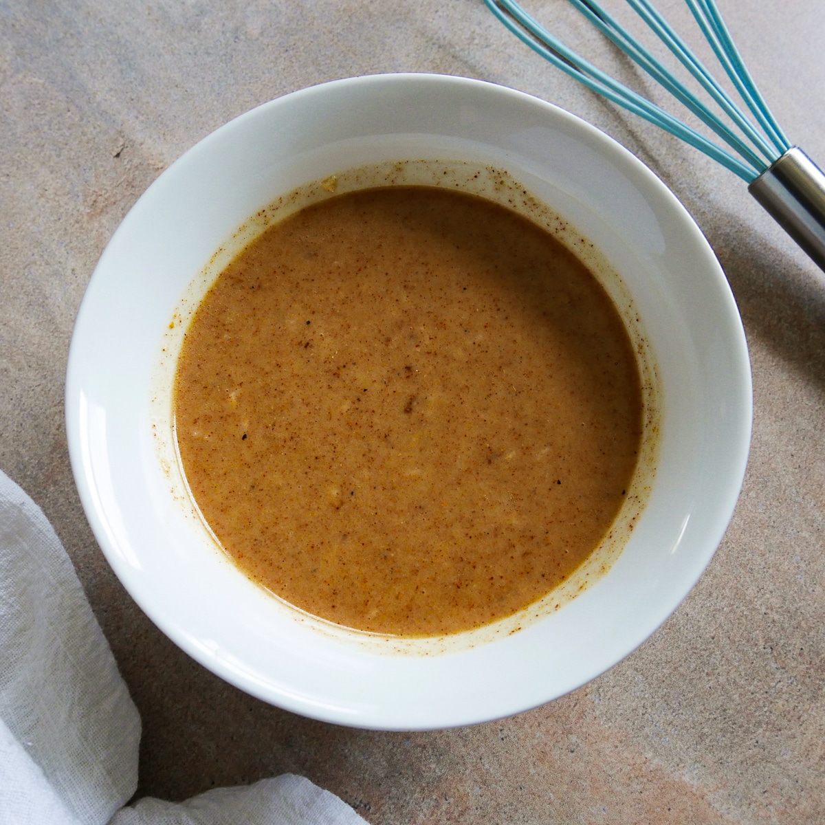 yogurt, oil, and Indian spices whisked together in a small bowl with whisk in background. 