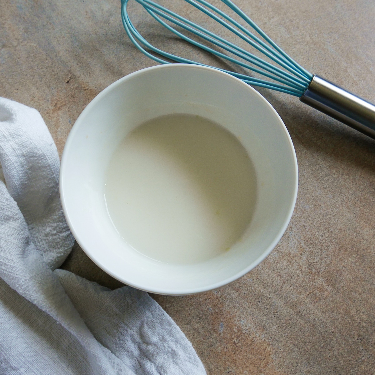 yogurt sauce in a small white bowl with whisk and napkin. 