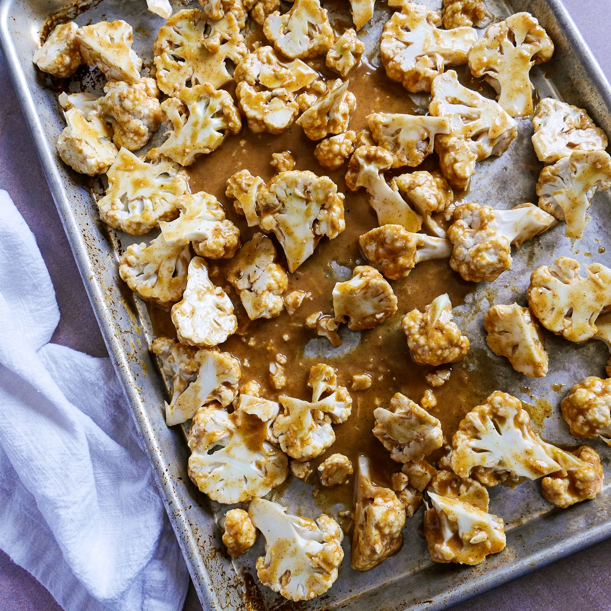 Marinated cauliflower spread out on a baking sheet with parchment paper. 