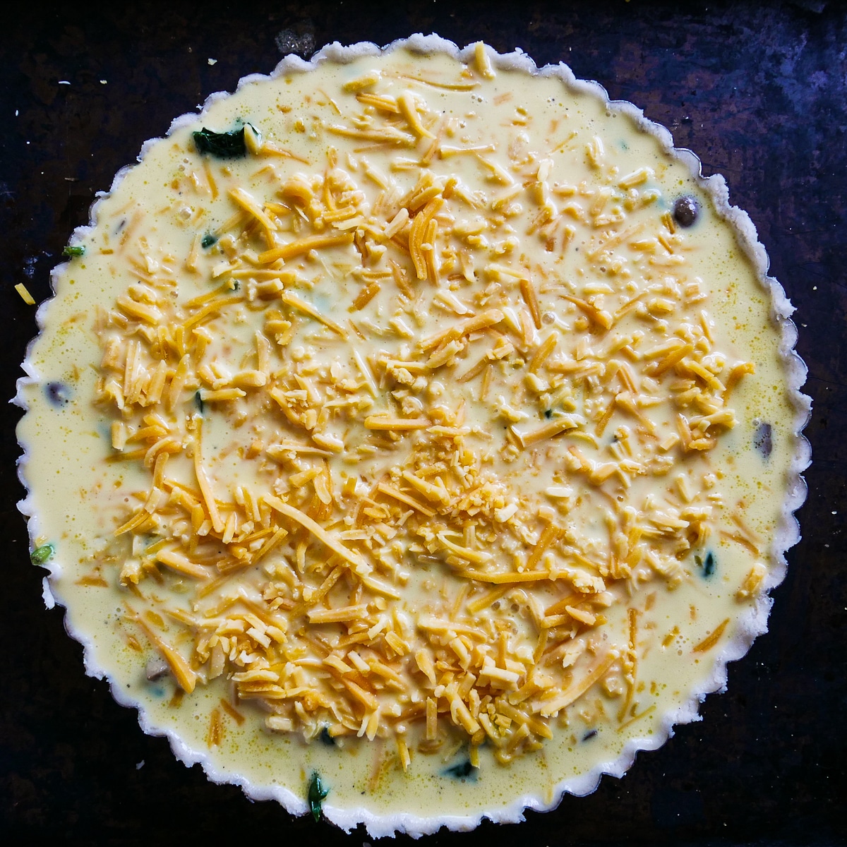 Egg mixture poured on top of vegetables in a tart pan and topped with cheese.