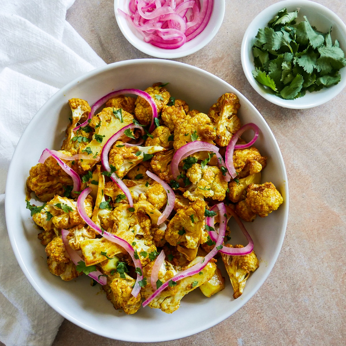 Cauliflower in a serving bowl with fresh cilantro and pickled onions on the side. 