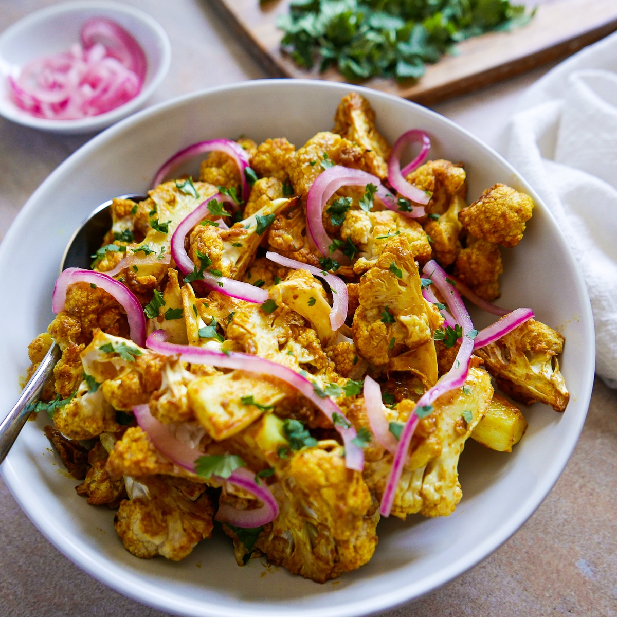 roasted cauliflower in a white bowl with pickled onions, cilantro, and a spoon. 