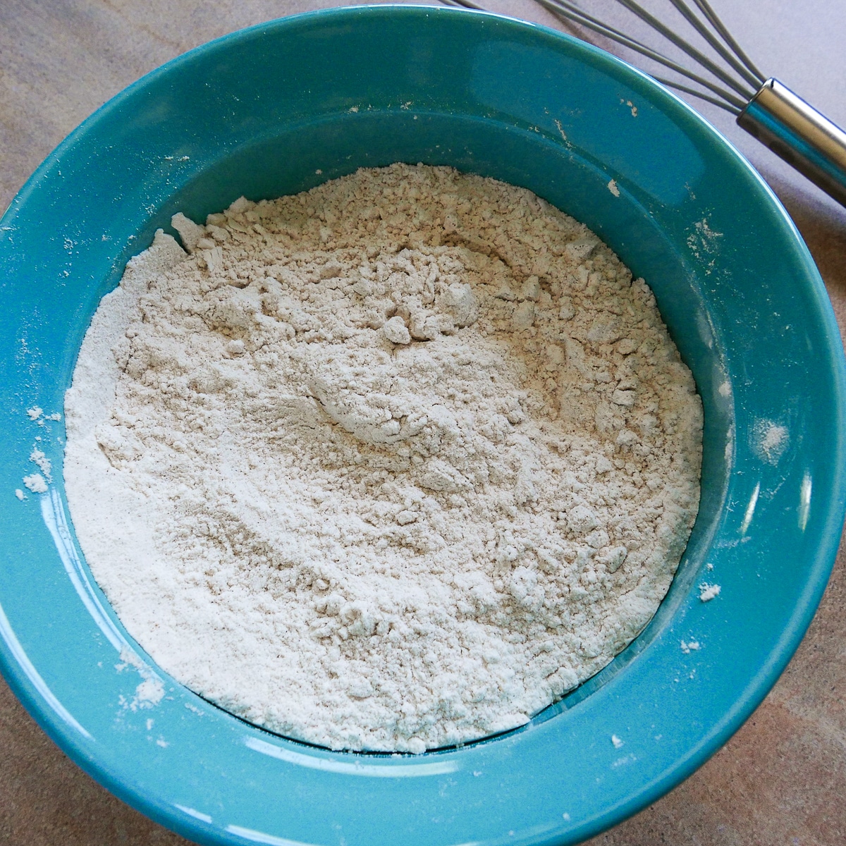 Dry ingredients mixed together in a blue bowl with whisk in the background. 