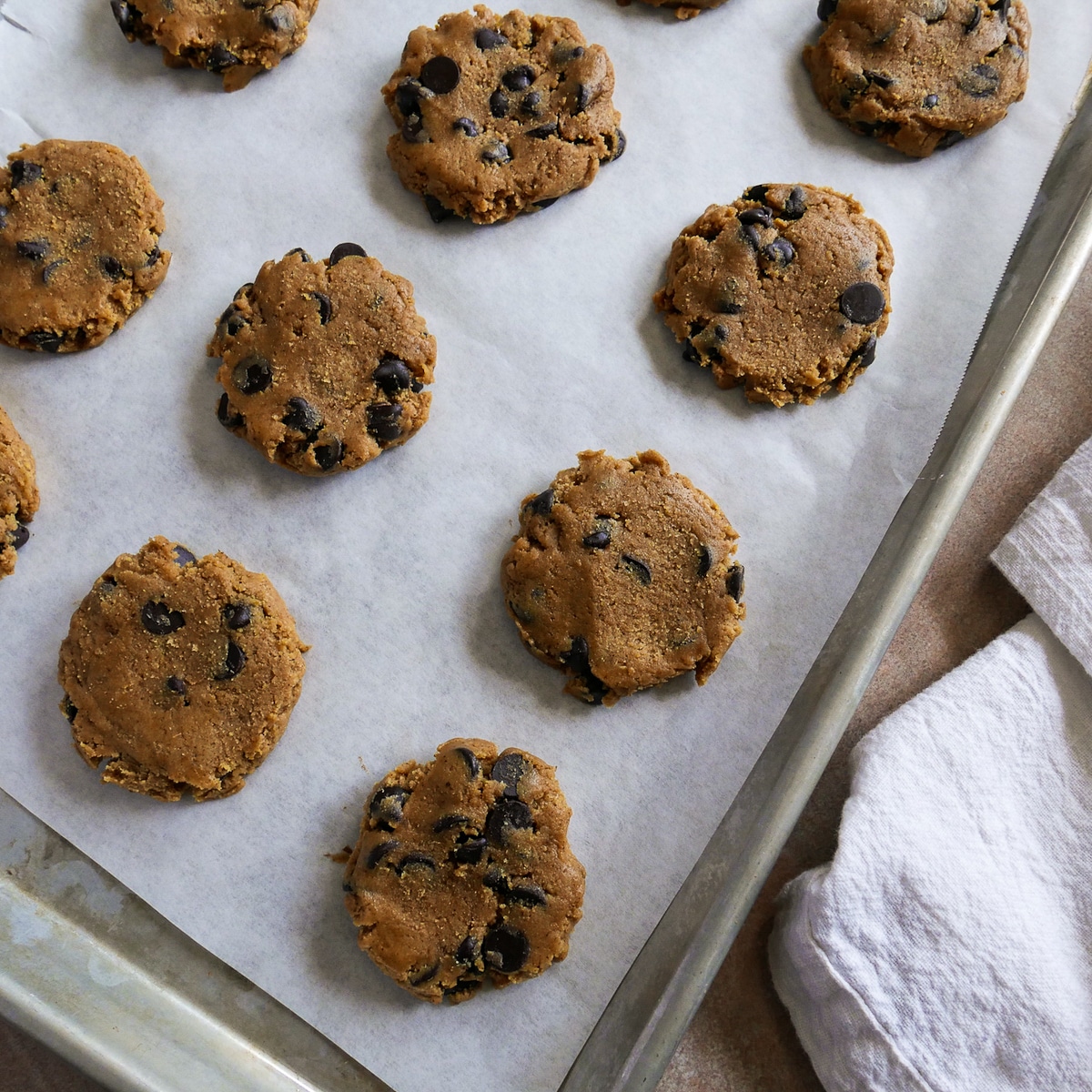 Cookie dough scooped onto parchment paper-lined baking sheet and pressed down.