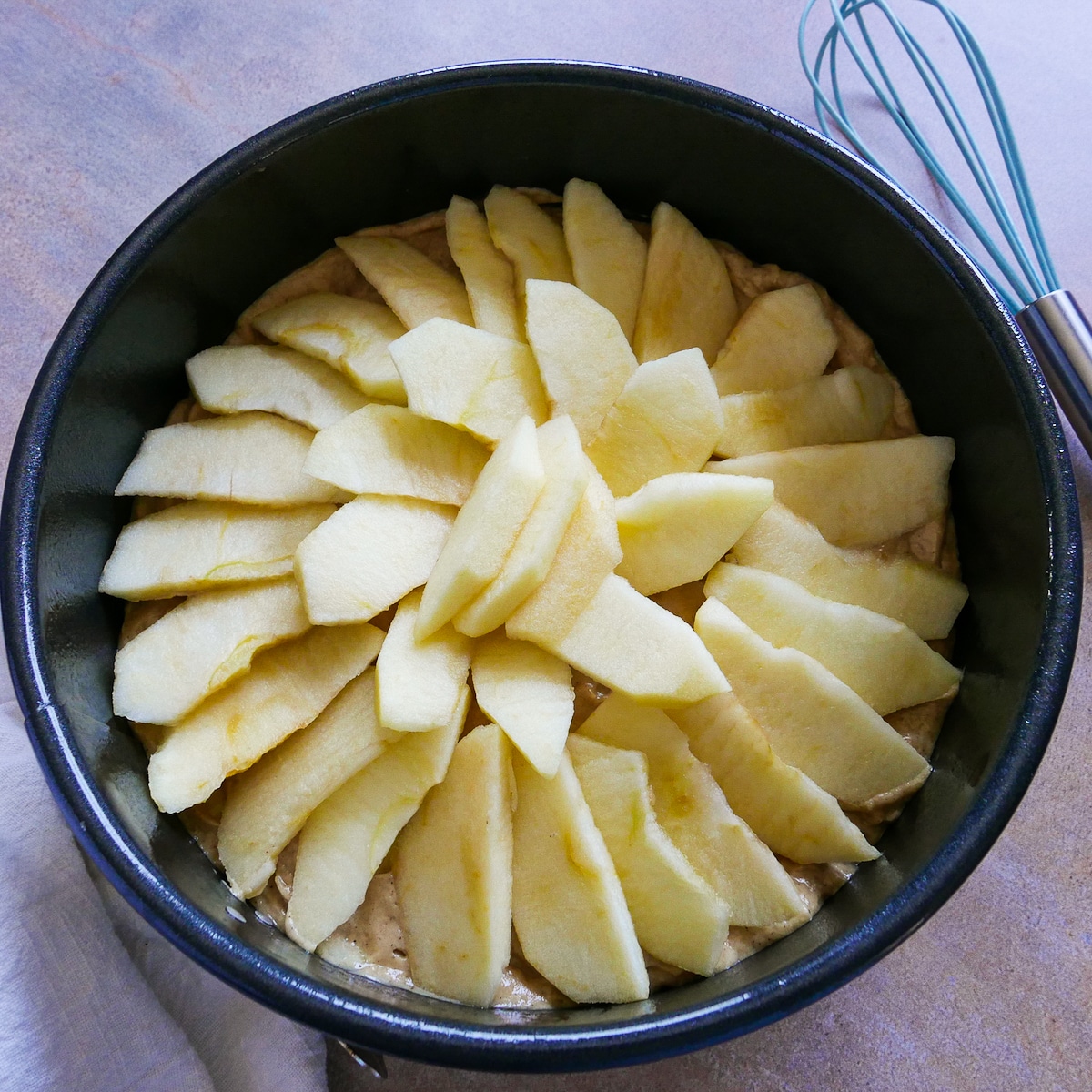 Apple slices arranged on top of cake batter in a springform pan with a white napkin.