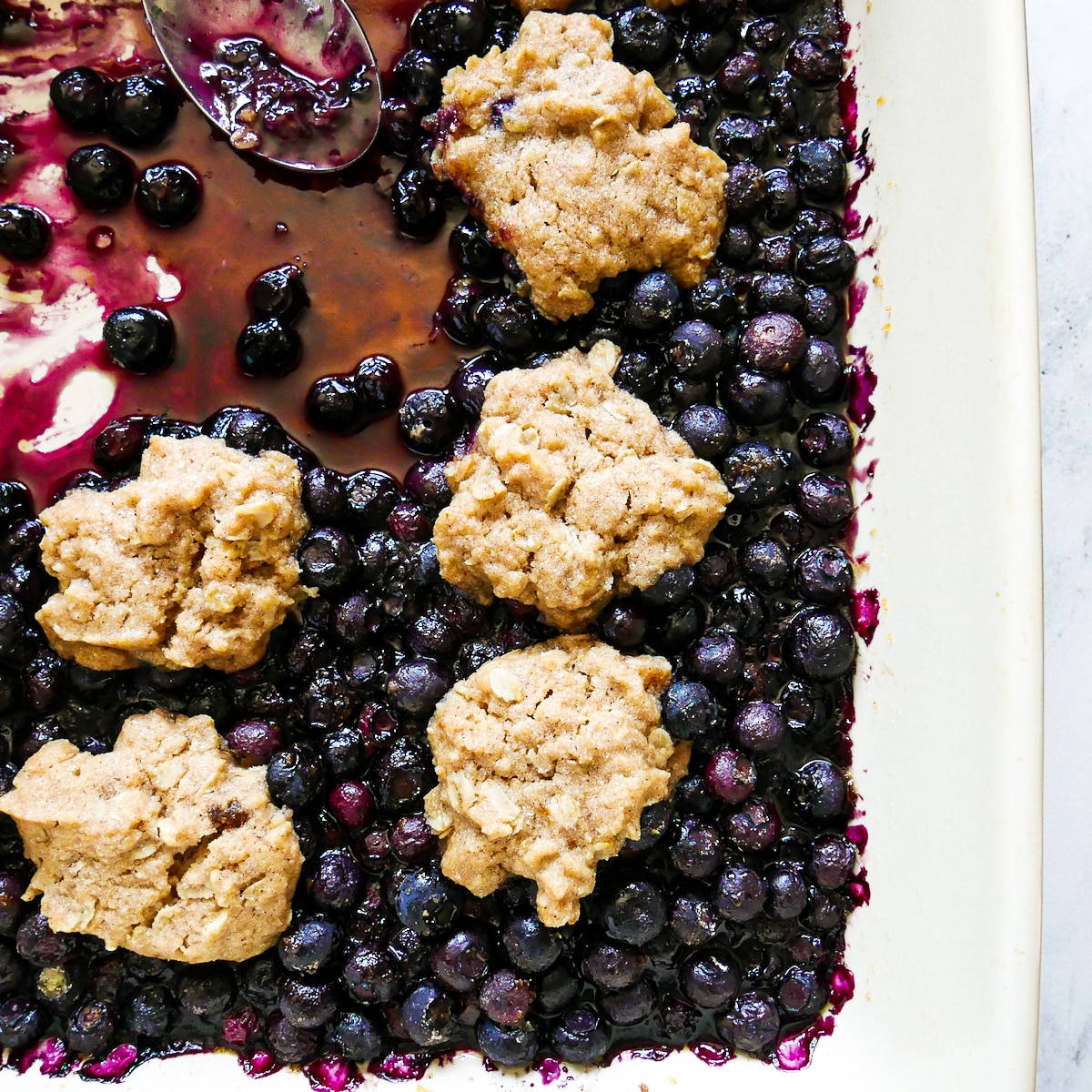Jammy blueberry cobbler in a large baking dish with spoon.