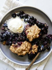 plate of blueberry cobbler with ice cream and a spoon resting on a white napkin.