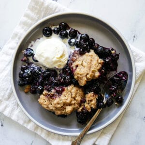plate of blueberry cobbler with ice cream and a spoon resting on a white napkin.