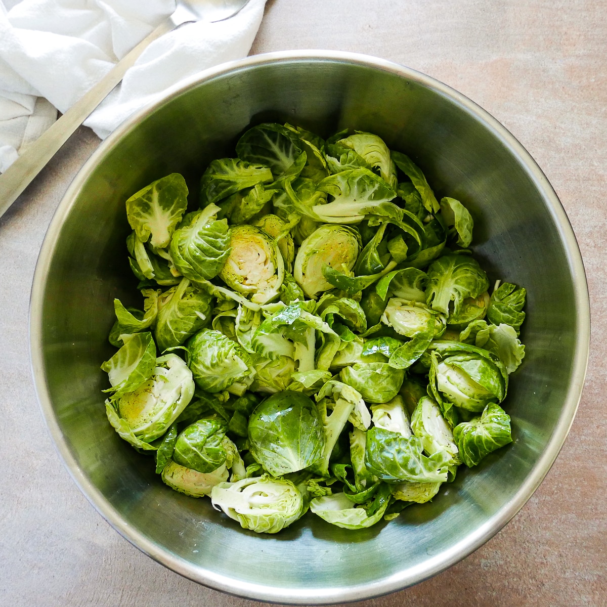Halved brussels sprouts tossed with olive oil, garlic, and seasoning in a mixing bowl. 