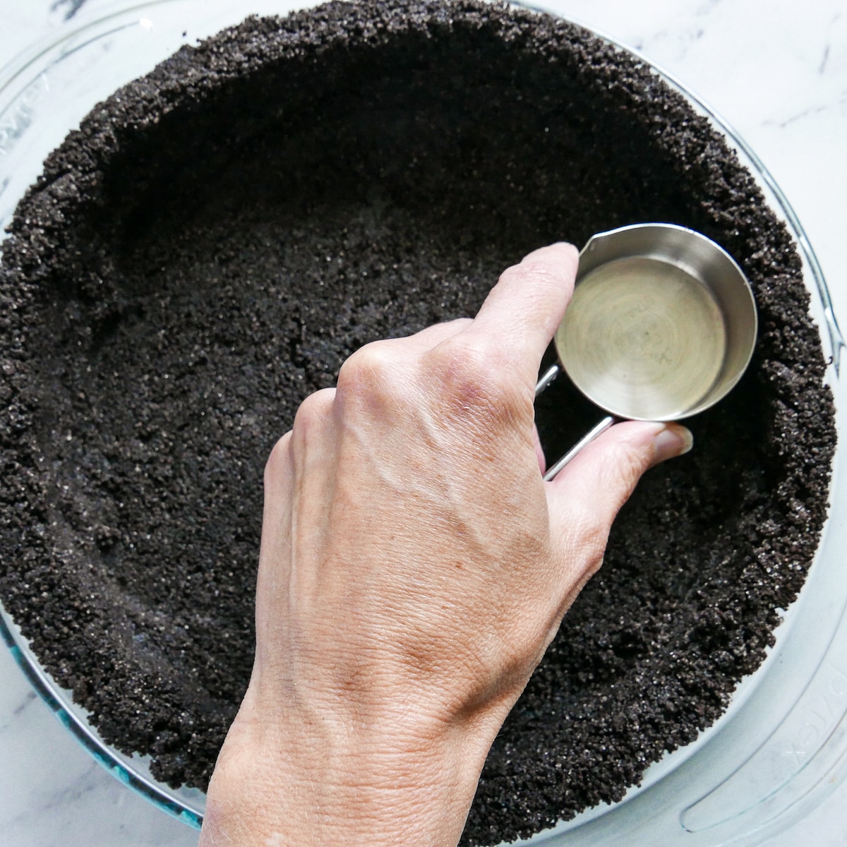 white hand pressing chocolate cookie crust into pie pan. 