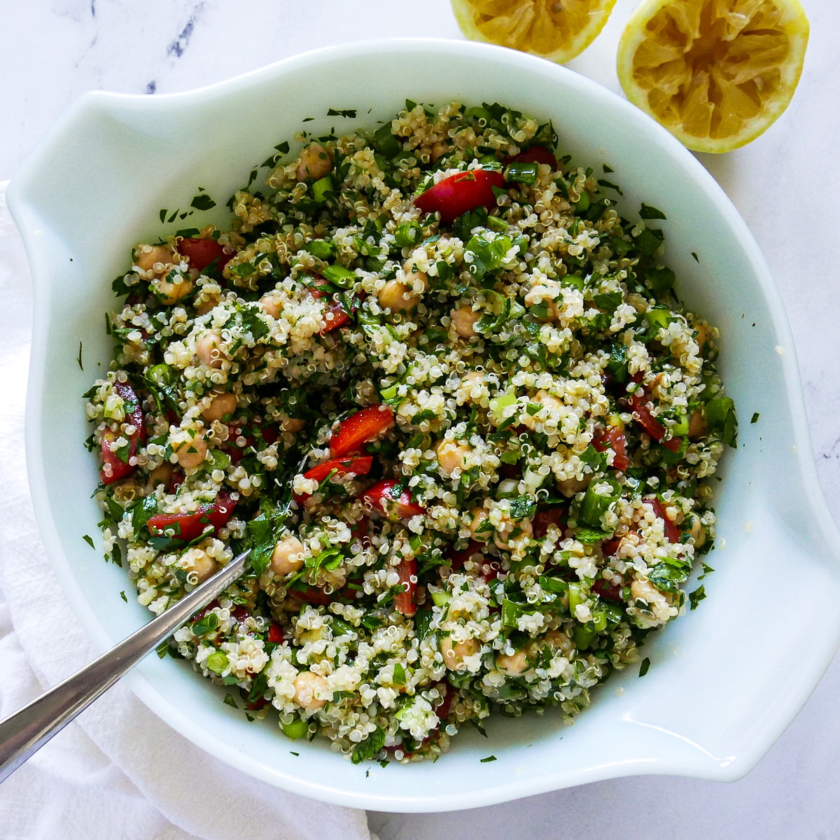 tabbouleh ingredients mixed together in a large bowl with spoon and lemon halves in background.