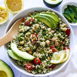 large bowl of gluten free tabbouleh garnished with avocado and lemon slices with a wooden spoon.
