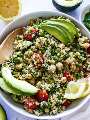 large bowl of gluten free tabbouleh garnished with avocado and lemon slices with a wooden spoon.