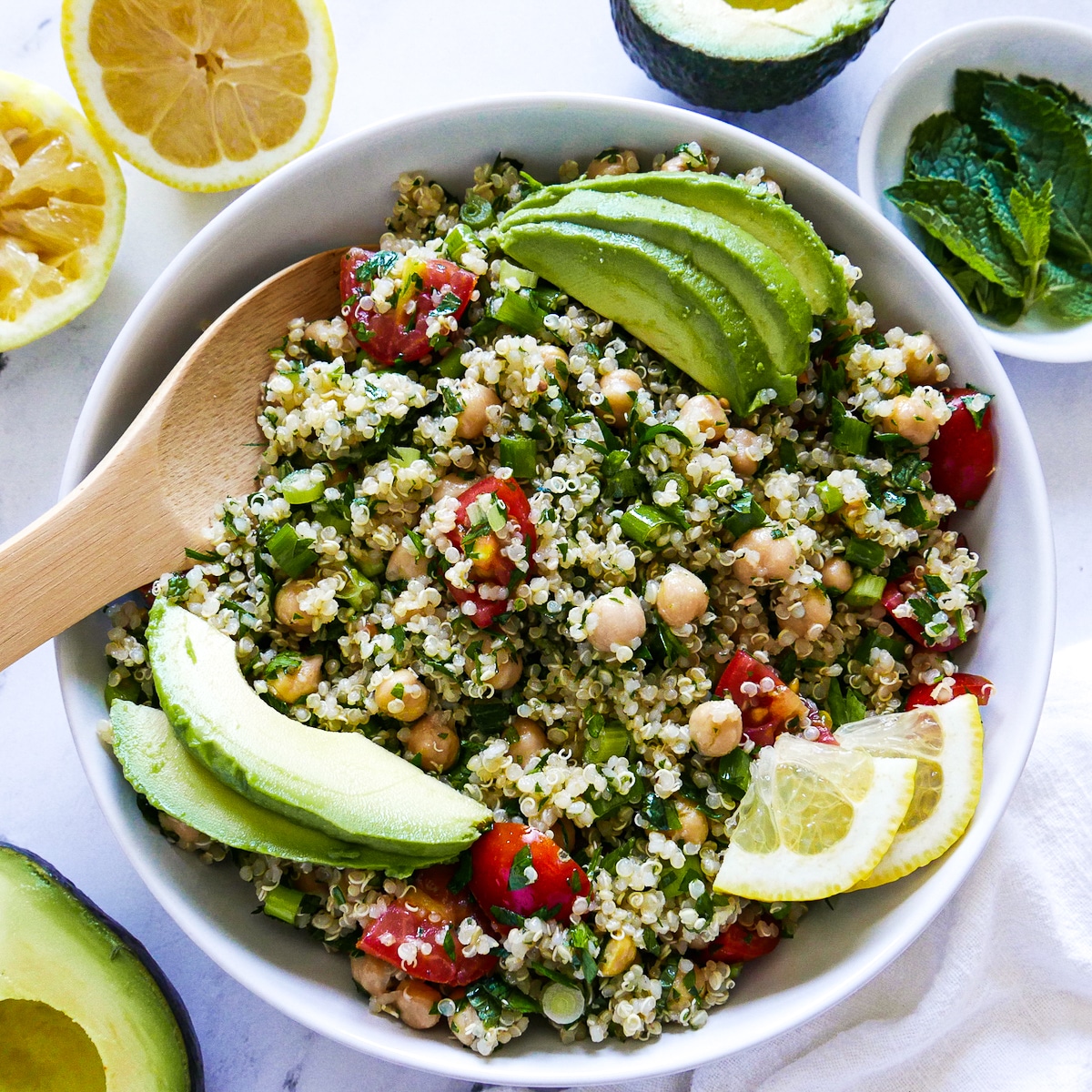 bowl-of-gluten-free-tabbouleh.jpg large bowl of gluten free tabbouleh garnished with avocado and lemon slices with a wooden spoon.