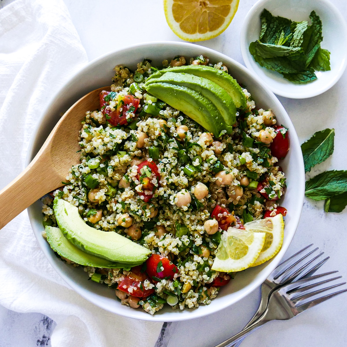 bowl of tabouli with wooden spoon and two forks on the side.