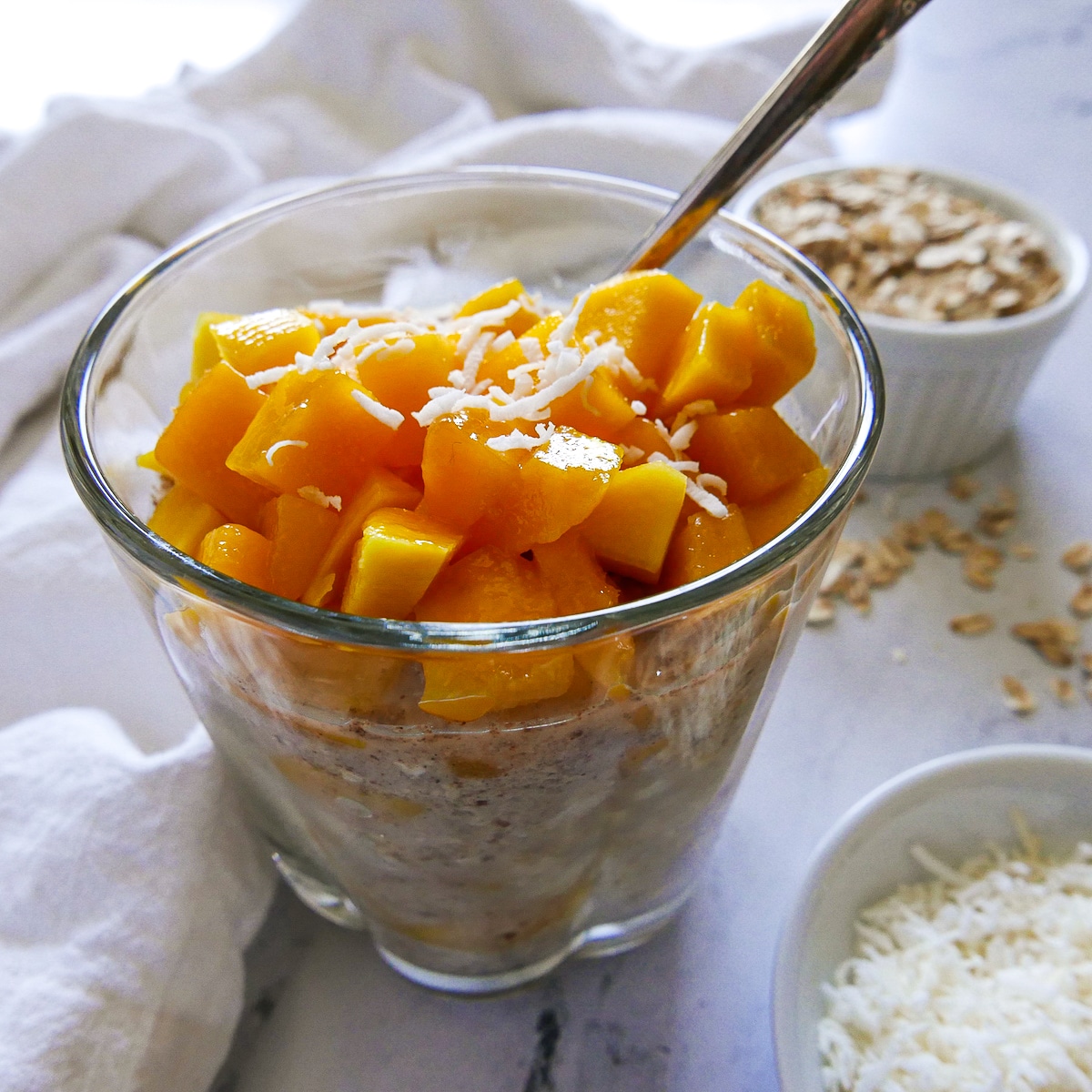 cup of overnight oats topped with fresh mango and a spoon. 