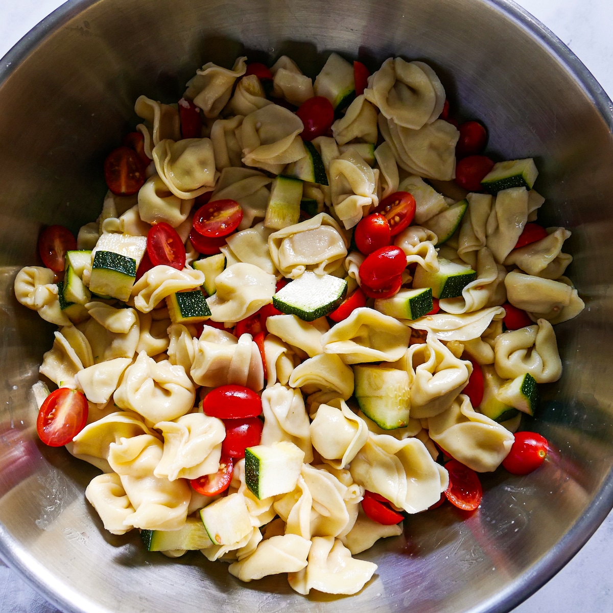 tortellini in a large bowl tossed with cherry tomatoes and chopped zucchini.
