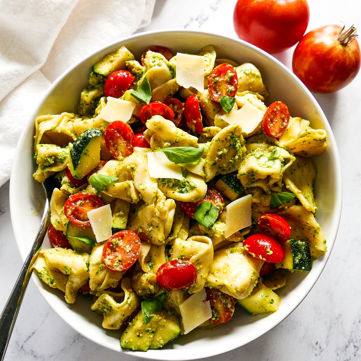 fork resting in a bowl of pasta salad with fresh basil and shaved parmesan. 