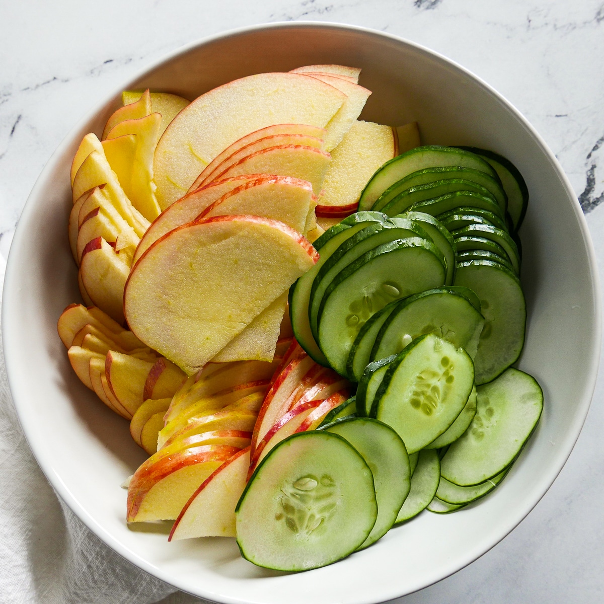 thinly sliced apples and cucumber in a mixing bowl.