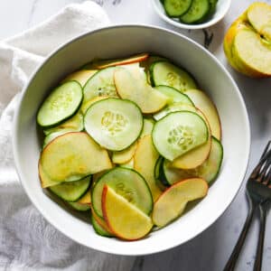 apple cucumber salad assembled in a bowl with two forks and napkin on the side.