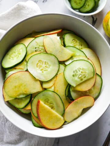 apple cucumber salad assembled in a bowl with two forks and napkin on the side.