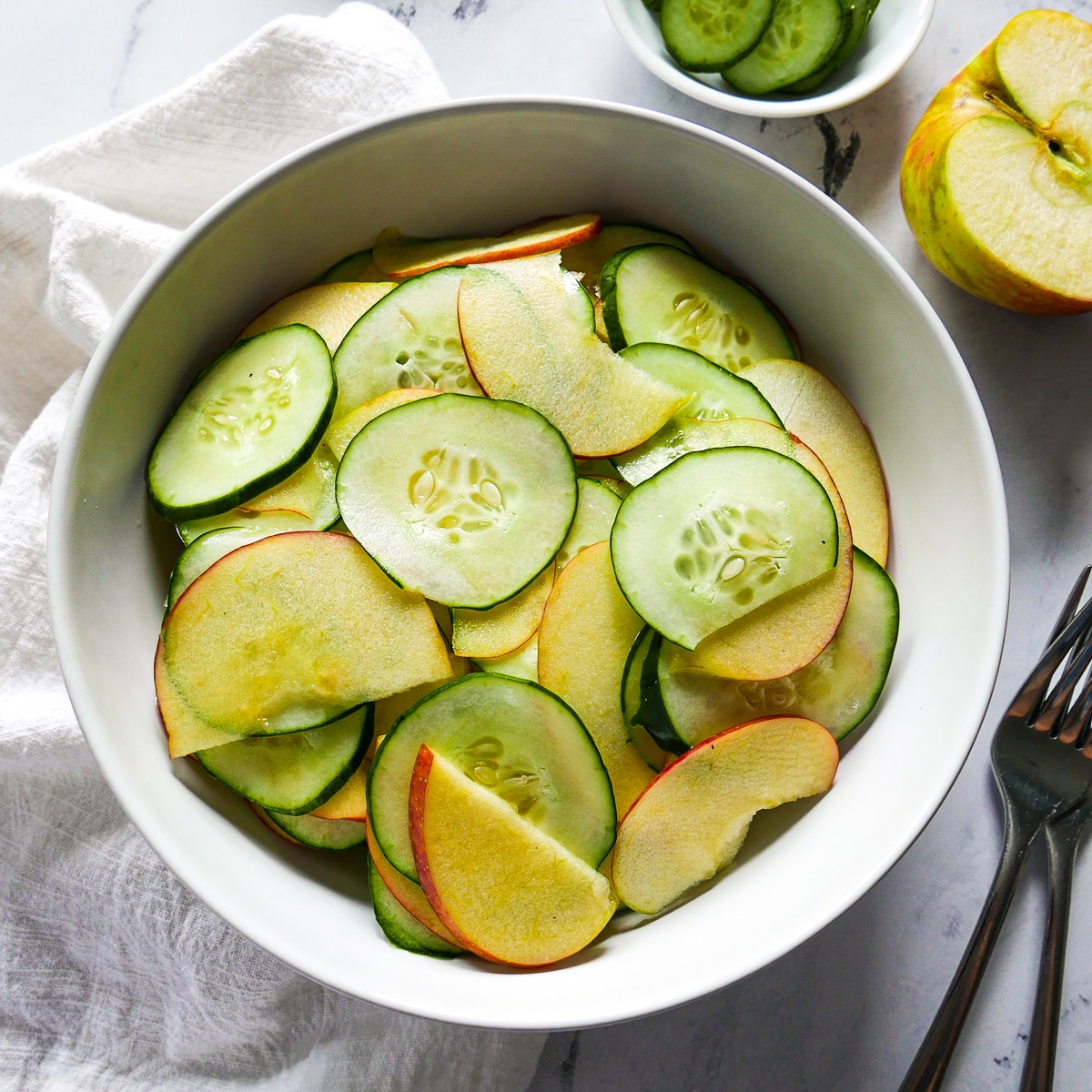 apple-cucumber-salad-assembled.jpg apple cucumber salad assembled in a bowl with two forks and napkin on the side.