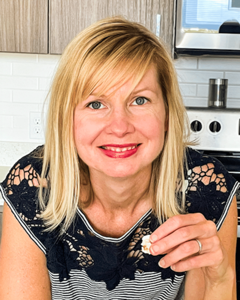 blonde woman standing in her kitchen eating popcorn. 