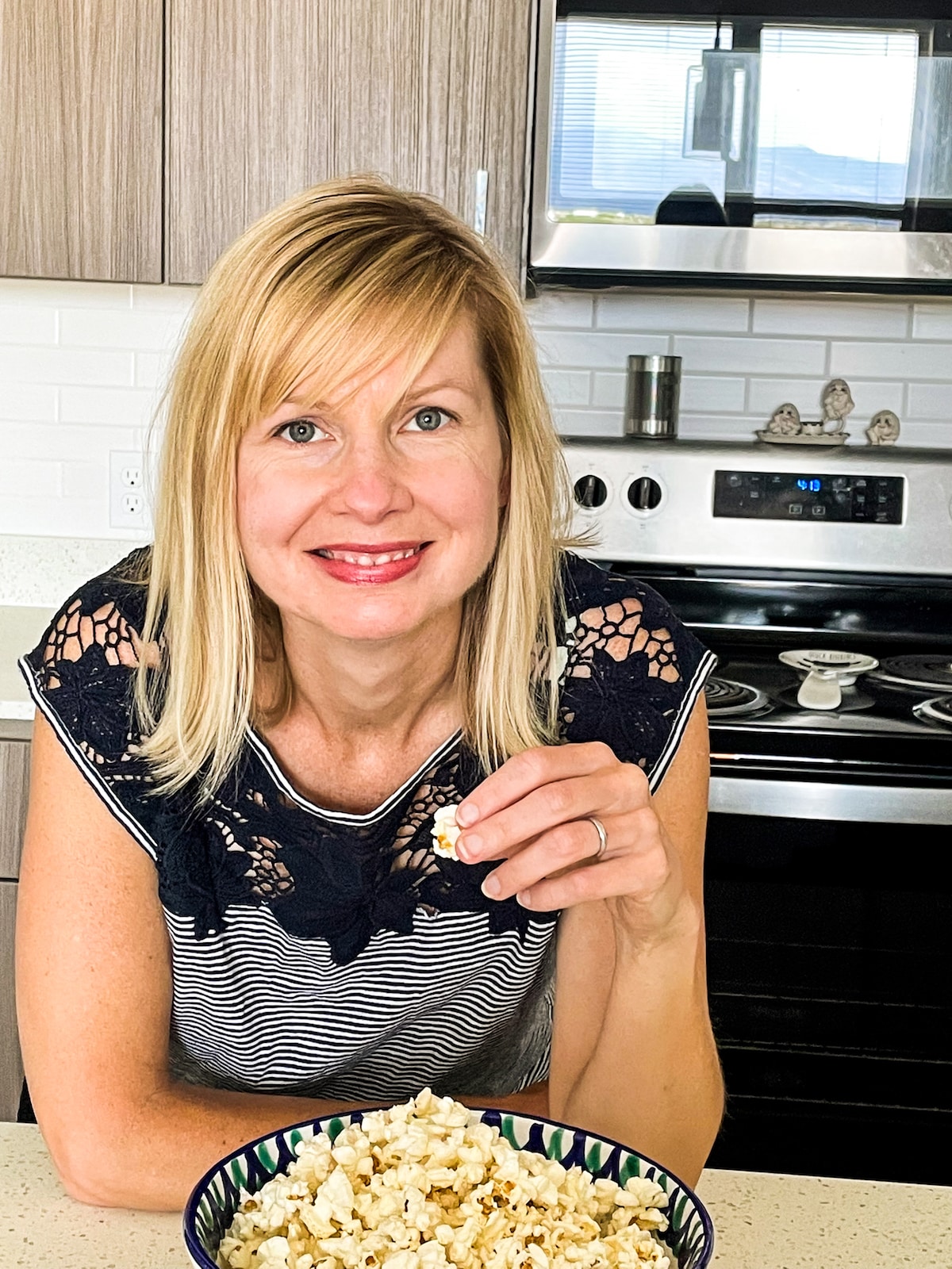 woman leaning over kitchen counter eating a bowl of popcorn.