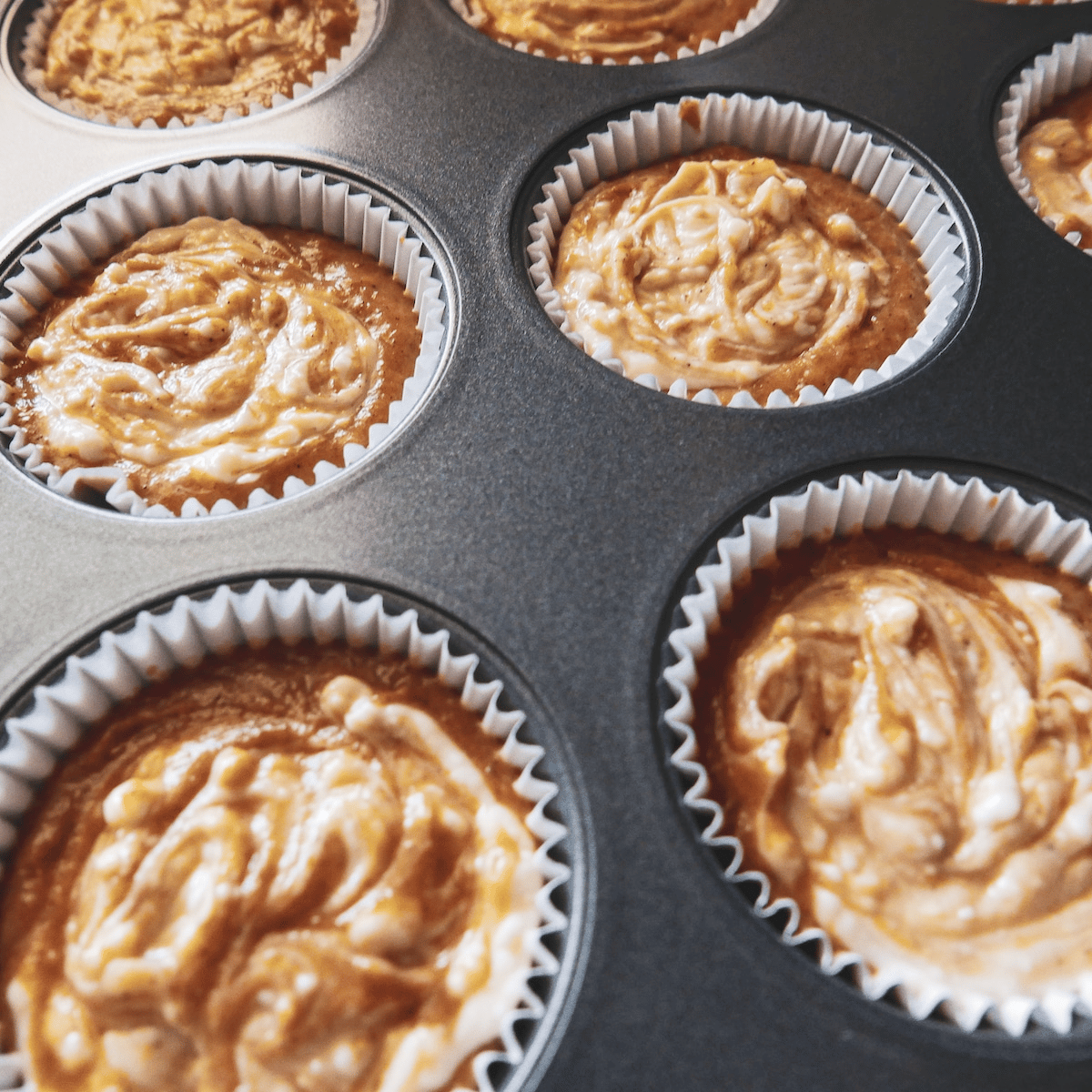 Cream cheese mixture swirled into muffin batter in a lined muffin tin. 