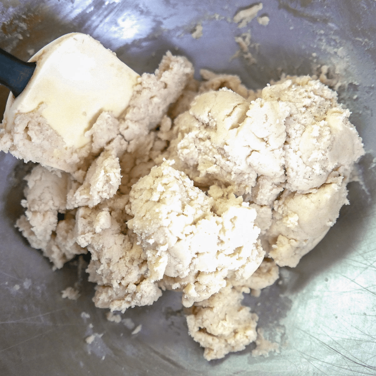 Rubber spatula mixing cookie dough in stand mixer bowl.