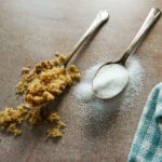 two spoons with brown sugar and white sugar and a napkin.