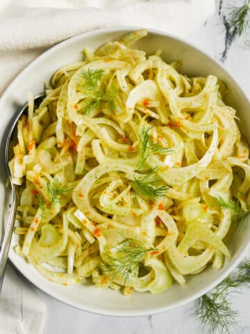 shaved fennel salad in a bowl with spoon and white napkin.