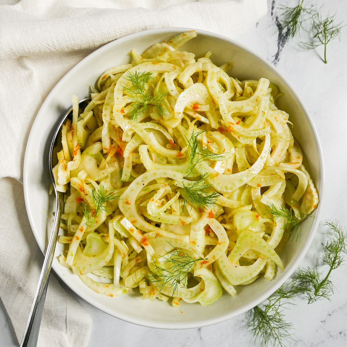 shaved fennel salad in a bowl with spoon and white napkin.