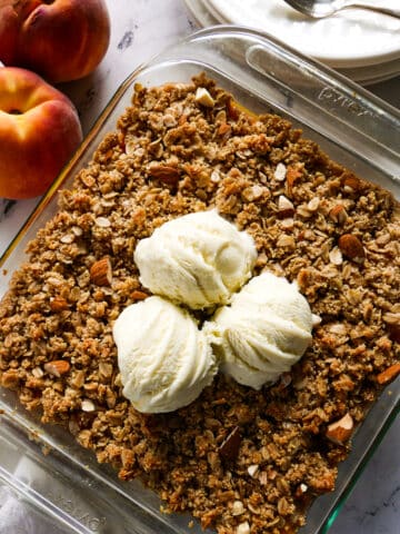 healthy peach crisp in a baking dish with three scoops of ice cream.