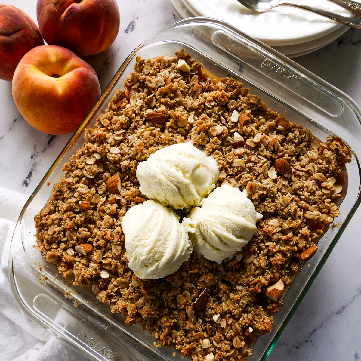 healthy peach crisp in a baking dish with three scoops of ice cream.