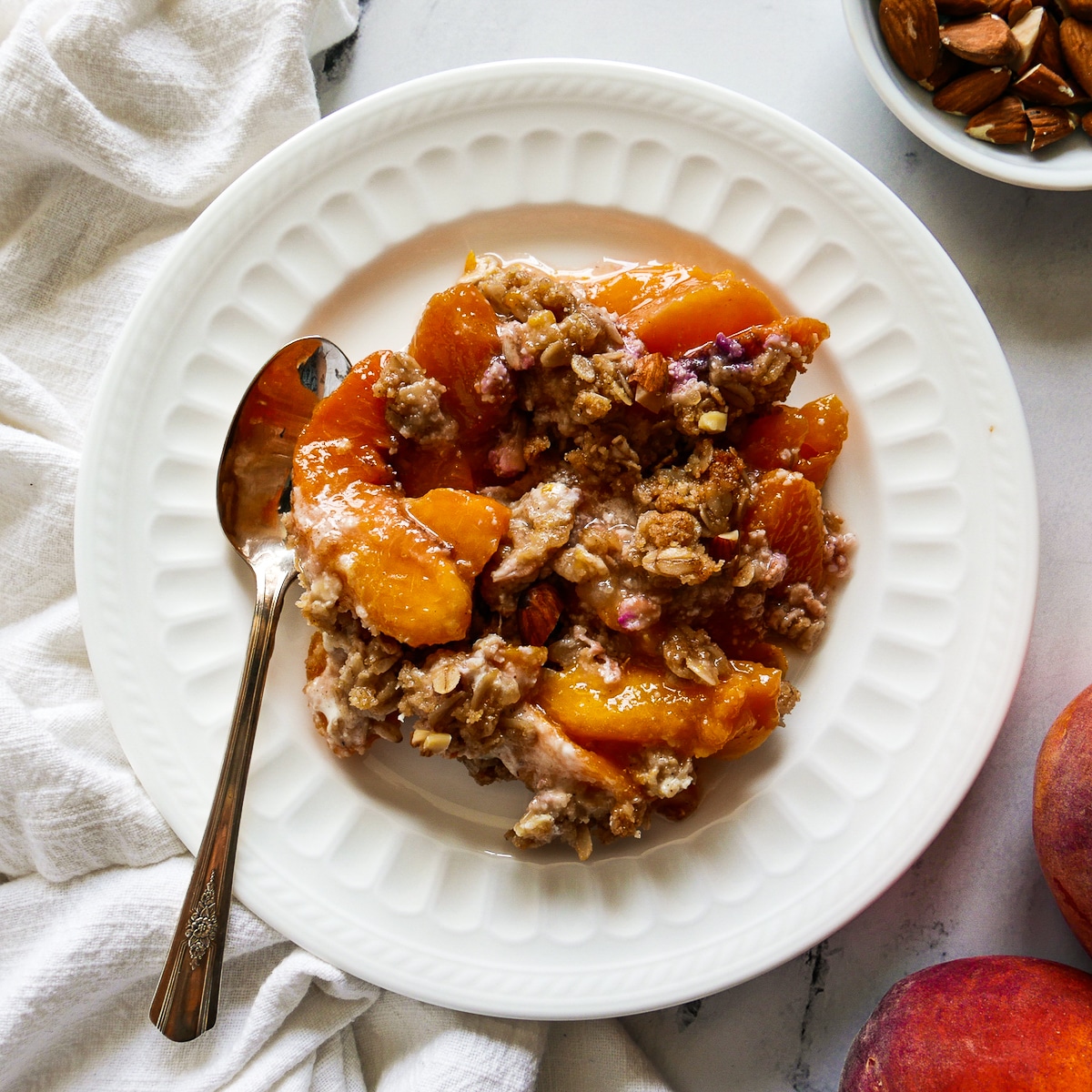 plate of peach crisp with a spoon and white napkin.