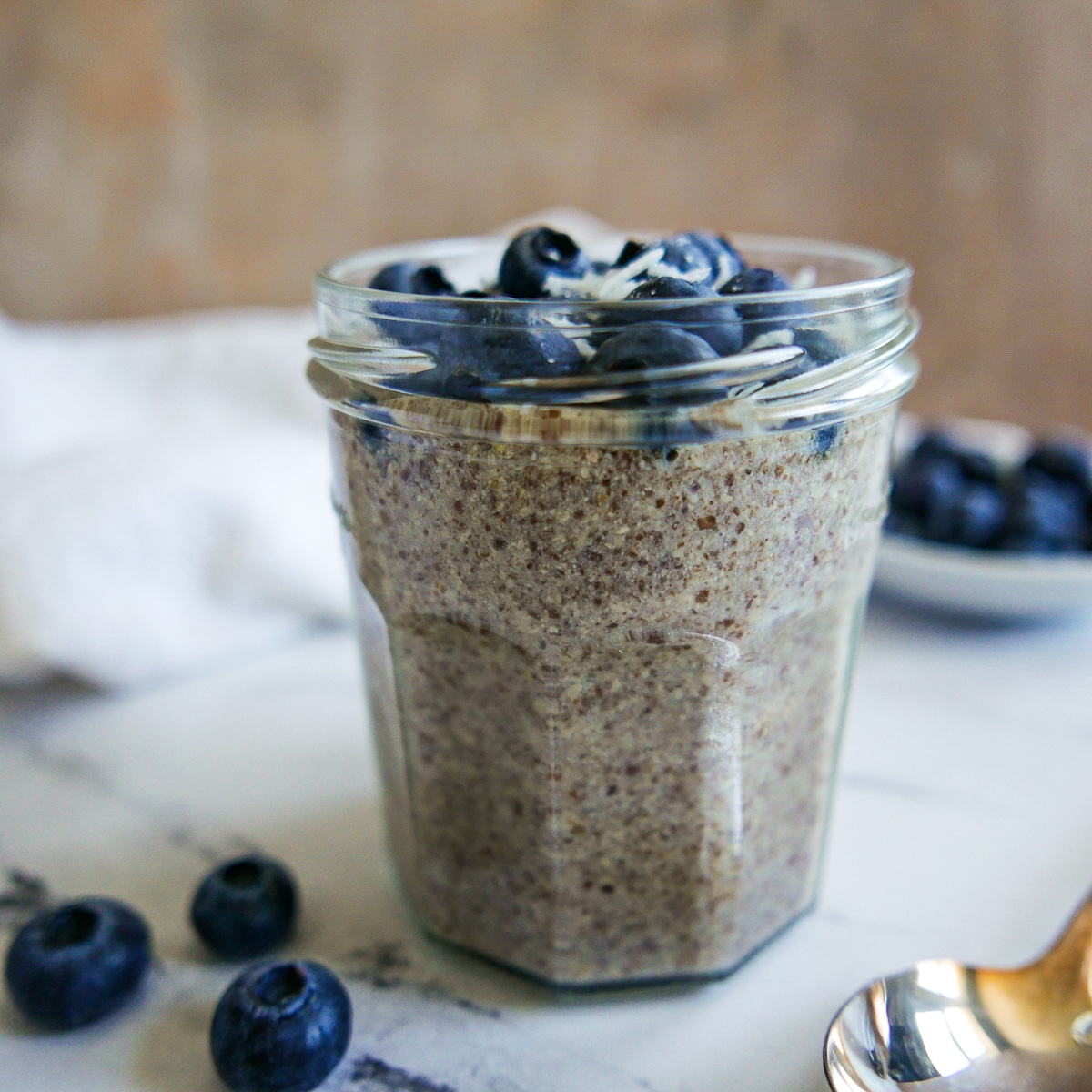 glass-of-pudding.jpg glass of flax pudding garnished with blueberries and blueberries in the background.