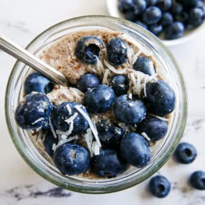 glass of creamy flaxseed pudding topped with blueberries and shredded coconut.