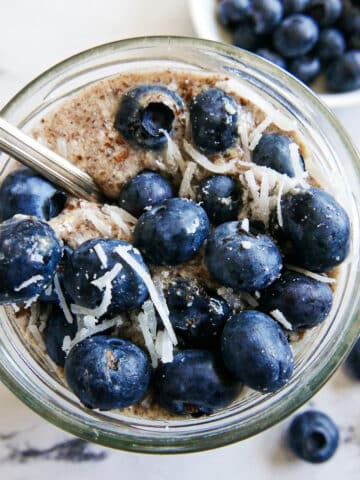 glass of creamy flaxseed pudding topped with blueberries and shredded coconut.