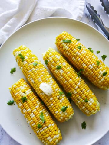 buttered corn on the cob resting on a white platter with tongs.