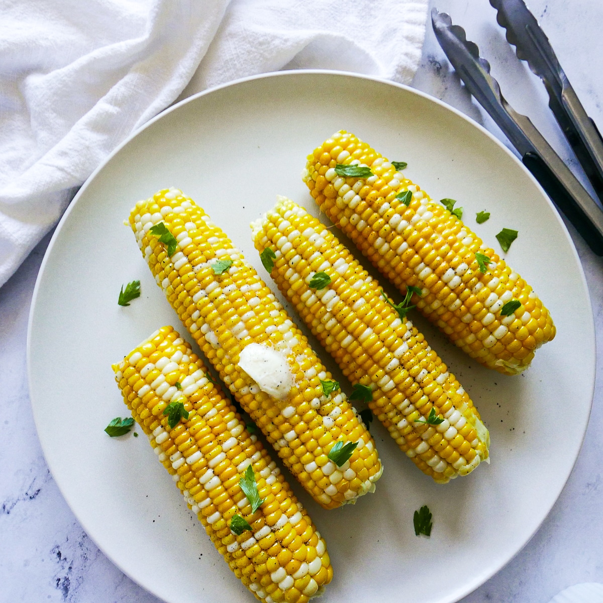 buttered corn on the cob resting on a white platter with tongs.