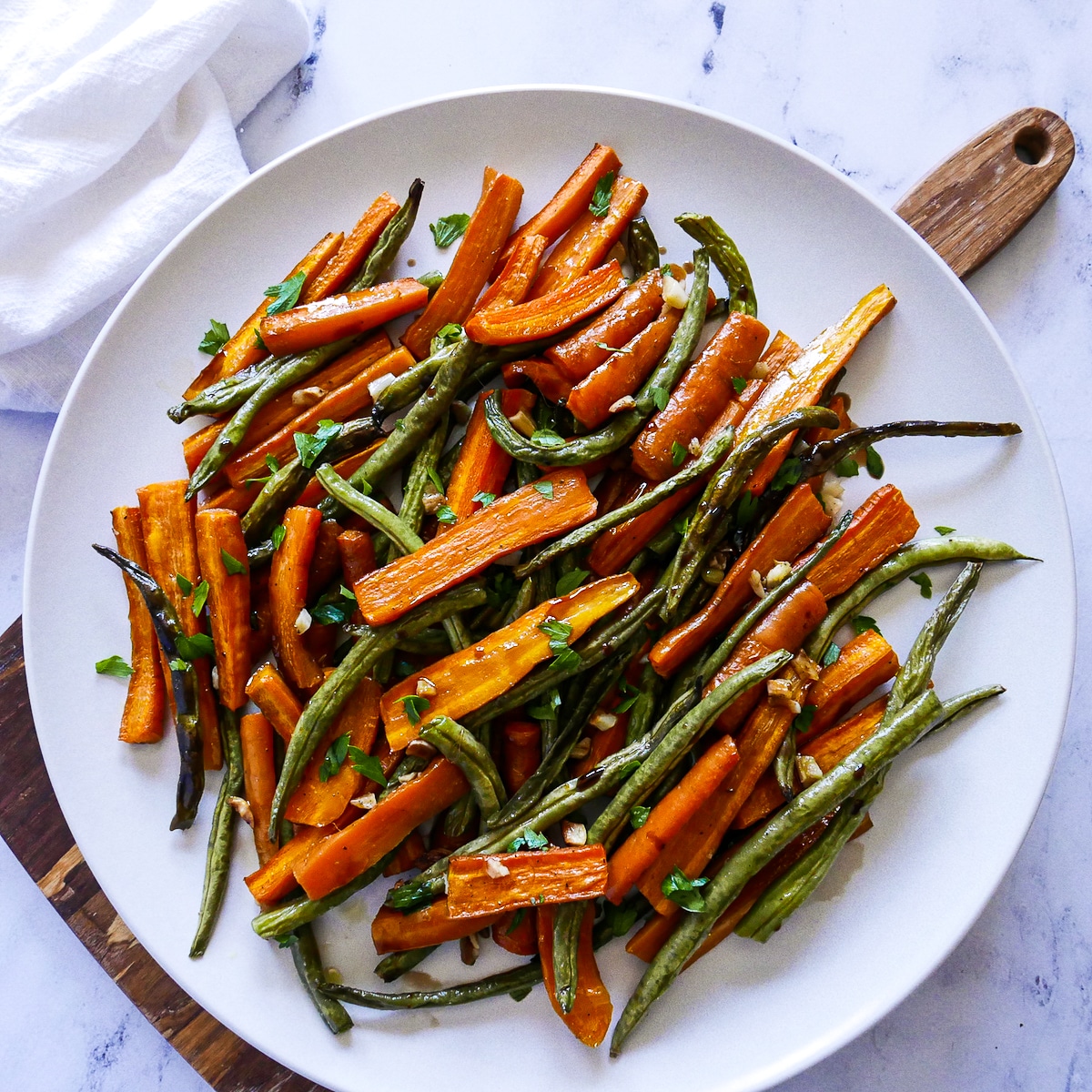roasted carrots and green beans on a white platter with napkin.