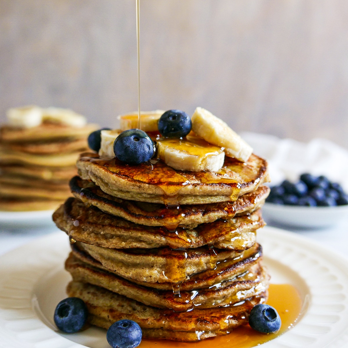 syrup-pouring-on-pancakes.jpg stack of banana oat pancakes with syrup being poured on top.