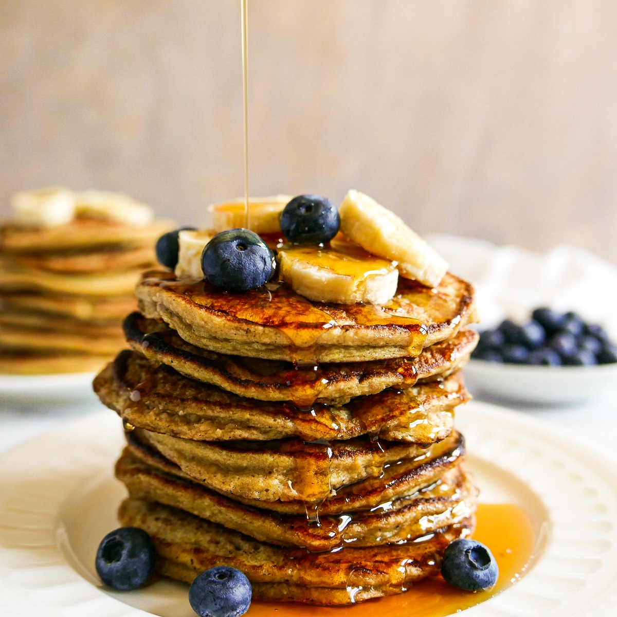 syrup-pouring-on-pancakes.jpg stack of banana oat pancakes with syrup being poured on top.